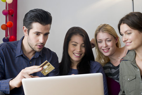 Friends gathered around laptop computer preparing to use credit card for online purchase