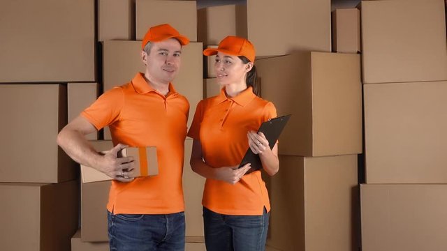 Couriers in orange uniform standing against brown cartboard boxes backround. Delivery company personel, 4K clip