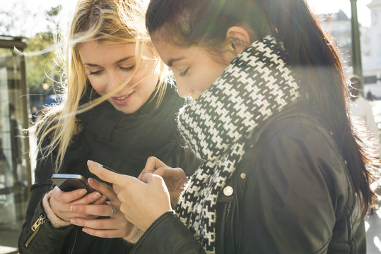 Young women together looking at their individual smartphones
