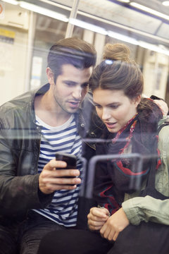 Young couple riding subway looking at digital tablet together