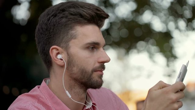Handsome man relaxing outdoors and listening music on earphones
