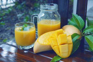 ripe yellow mango smoothie decorated by mint leaf on top with fruit and green leaf on wooden...