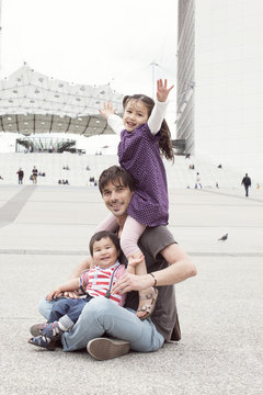 Father sitting on the ground with two children in city square