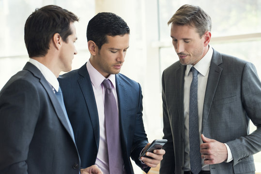 Businessman talking with colleagues, looking at smartphone