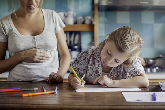 Mother looking at her daughter sketching on paper