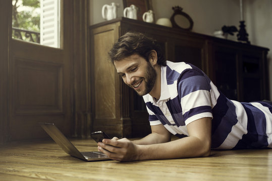 Man lying on floor using laptop and smartphone