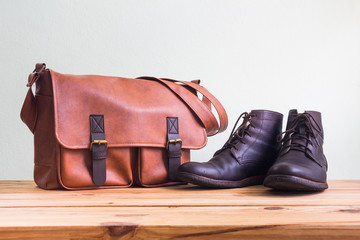 Men's fashion with brown leather bag and brown boots on wooden table over wall background