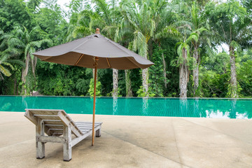 Wooden sunbed with umbrella beside on modern swimming pool in shady garden