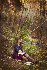 Beautiful young brunette sitting on a fallen autumn leaves in a park, reading a book