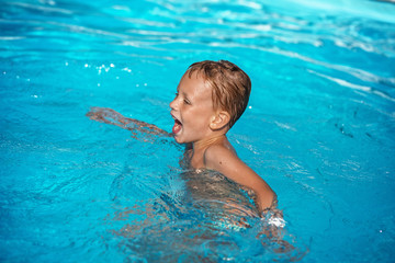 Fototapeta na wymiar Happy kid playing in blue water of swimming pool.