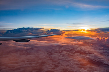 Fototapeta na wymiar Looking from window to Air plane Wing in Flight , with beautiful scenery of amazing cloud formations on sunset sky