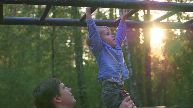 the father helps the child to climb on the horizontal ladder