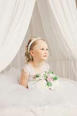 Little bride sitting on the bedl with bouquet