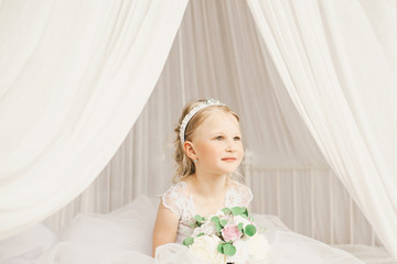 Fototapeta na wymiar Little bride sitting on the bedl with bouquet