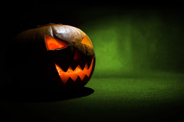 The carved face of pumpkin glowing on Halloween on green background