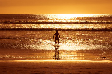 Piękny zachód słońca - chłopiec biega po wodzie nad oceanem