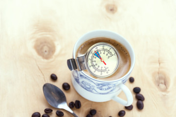 Espresso coffee cup. Use a thermometer measures the temperature before drinking placed on a wooden floor with a small spoon, and several coffee bean seeds.
