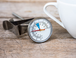 The thermometer for coffee and coffee cups placed on a wooden floor.