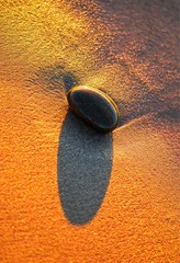 Morski kamyk rzucający długi cień na mokry piasek w kolorze zachodu słońca