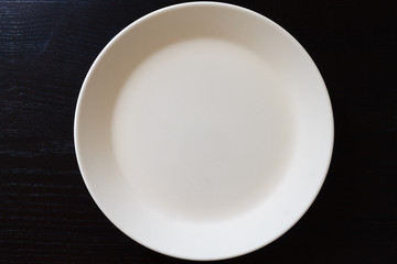 Empty white plate on black wooden table