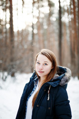 Stylish young woman in winter clothes standing in winter forest