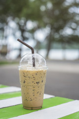iced coffee in takeaway cap on wooden table,blurred sea in background,selective focus