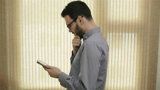 A man in glasses using a tablet and thinking.