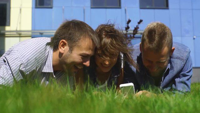 three students lying on the lawn and use the phone
