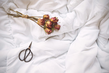 Dry roses and vintage scissors on bed