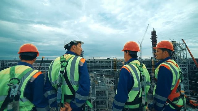 Workers at refinery as team discussing, industrial scene in background.