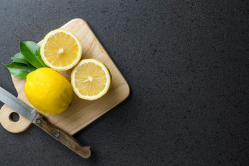The lemons are on top of wood cutting board with knife. Top view