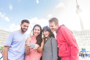 Group of friends looking at smart phone in Berlin. Mixed race group with caucasian, middle eastern and nordic persons, standing in Alexanderplatz. Happiness and friendship concepts.