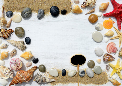 Seashells, starfish, pebbles and empty black plate for text on a white wooden background
