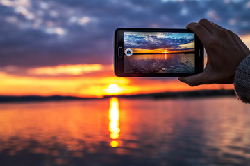 Naklejka premium kobieta ręce trzymając telefon komórkowy o zachodzie słońca.