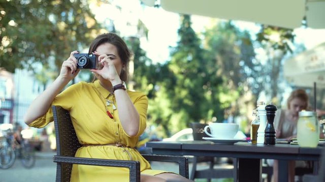 Woman sitting in the outdoor cafe and doing photos on old, vintage camera
