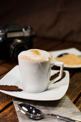 Cup of coffee (machiatto) on desk while there are sugar and vintage camera in background