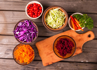 Selection of autumn vegetables, rich in vitamins. Set for cooking fresh salad or vegetable stew. In the glass, ceramic and clay bowls on a wooden table, top view. Next to the cutting board