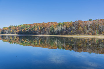 Fototapeta na wymiar The last colors of late fall mirror reflect on the calm water of Moreau Lake.