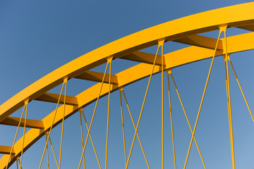 Yellow bridge against a steel blue sky showing beams, girders, columns and cables