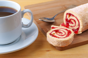 Sweet roll with jam and tea spoon on a cutting board. Cup of tea on a wooden table.