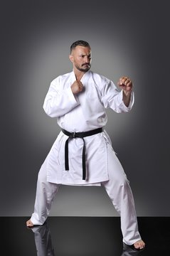 Handsome young male karate doing kata on the gray background