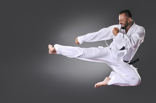 Handsome young black belt male karate doing kick on the gray bac