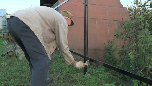 Adult man paints the iron fence using black paint
