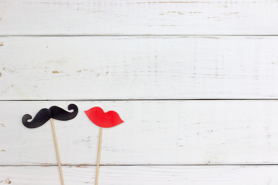Paper heart shape fake mustaches in sticks in front of wooden white background. Wedding concept.