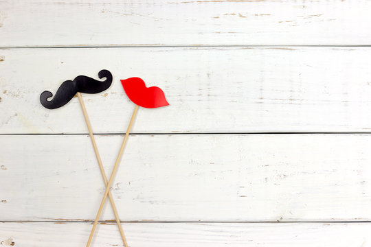 Paper heart shape fake mustaches in sticks in front of wooden white background. Wedding concept.