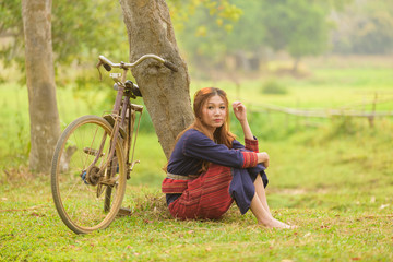Young asian women sitting next to tree with bike in rice field a