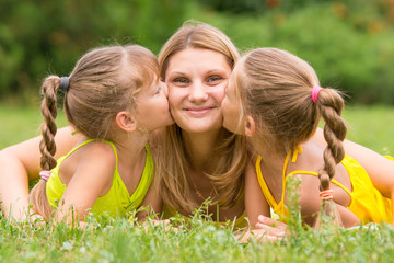 Two daughters kissing mother lying on the grass on a picnic