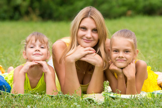 Mother and two daughters lie on the green grass and propping up hands a head looked in the picture