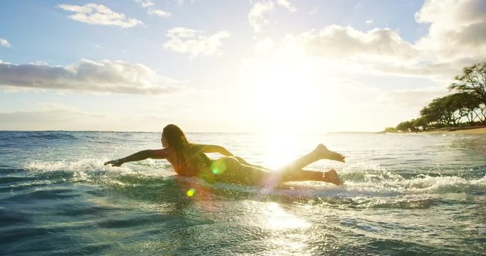 Beautiful surfer girl running into the ocean at sunset