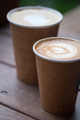 Two cups of latte art with heart shape in brown paper cup. selective focus